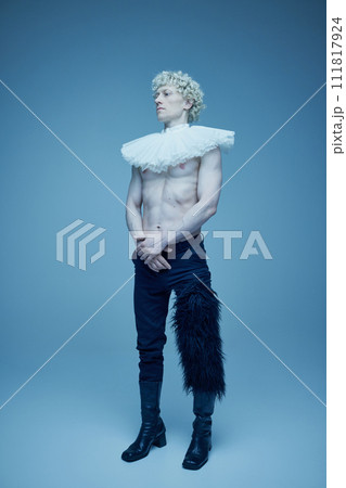 Past and present. Full length portrait of shirtless man with ruffled collar and black trousers against blue studio background. 111817924