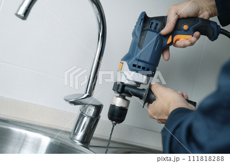 man drilling a hole in a metal sink 111818288