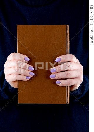 A brown hardback book in female hands with a fashionable manicure. 111818383