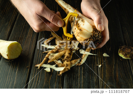 Making a sweet beetroot drink or smoothie at home. Close-up of man hands peeling raw sugar beets with a vegetable peeler Making a sweet beetroot drink or smoothie at home. Close-up of man hands peeling raw sugar beets with a vegetable peeler 111818707