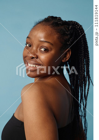 Vertical medium closeup of self-confident African American girl with braided hair posing for camera in studio, baby blue background Vertical medium closeup of self-confident African American girl with braided hair posing for camera in studio, baby blue background 111819144