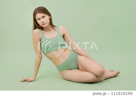 Horizontal studio portrait of young Caucasian woman wearing comfortable ribbed underwear posing for camera, mint green background 111819280
