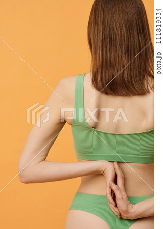 Rear view studio shot of unrecognizable Caucasian woman with brown hair wearing pale green underwear posing for camera with hands behind her back Rear view studio shot of unrecognizable Caucasian woman with brown hair wearing pale green underwear posing for camera with hands behind her back 111819334