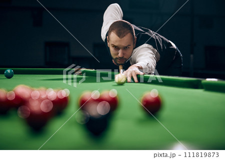 Concentrated young man leaning on billiards table, playing snooker game. Lifestyle magazine spread highlighting leisure activities 111819873