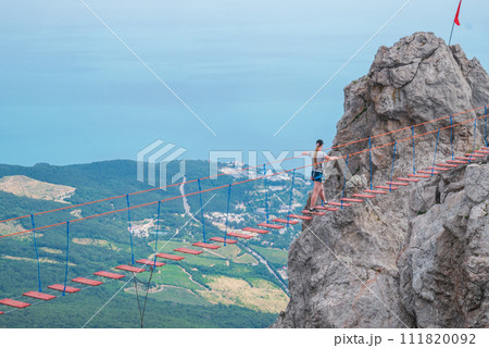 The girl walks on the suspension bridge between the tops of the mountains. 111820092