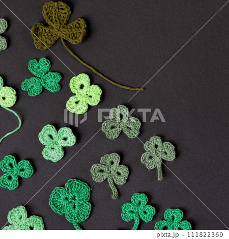 St Patrick's Day concept. Composition made of knitted green shamrocks on a black background. Holiday sign and knitted clover leaf. 111822369