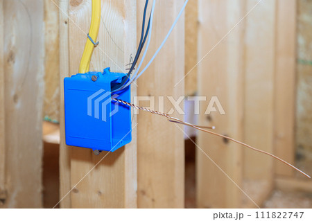 Plastic electrical switch box with wires at wooden frame beams on wall 111822747