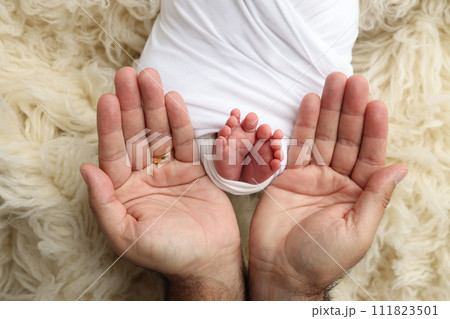 The palms of the father, the mother are holding the foot of the newborn baby in a white blanket. Feet of the newborn on the palms of the parents. Studio macro photo of a child's toes, heels and feet. 111823501