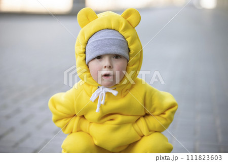Funny little girl in a warm yellow suit with ears on a walk. 111823603