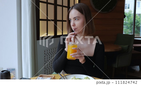 A woman eats in a cafe, a beautiful young girl has lunch in a restaurant. A business woman is having dinner in a cafe and drinking freshly squeezed juice. Young woman in a cafe 111824742