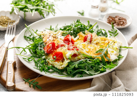 Fried eggs, omelette with onions, tomatoes and fresh arugula salad Fried eggs, omelette with onions, tomatoes and fresh arugula salad 111825093