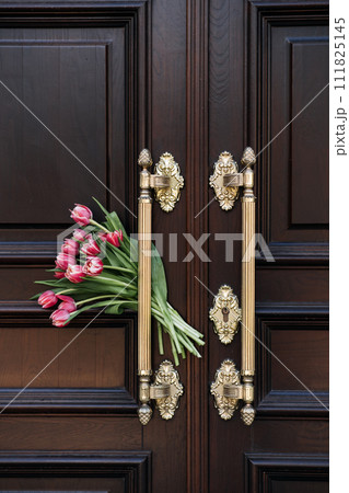 Welcome and Hospitality. Tulips bouquet Beside Ornate Wooden Door Welcome Symbol. The flowers next to a door symbolize a warm welcome or hospitality in home or upscale venue. Welcome and Hospitality. Tulips bouquet Beside Ornate Wooden Door Welcome Symbol. The flowers next to a door symbolize a warm welcome or hospitality in home or upscale venue. 111825145