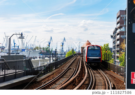 Hamburg Red U-bahn Subway train departure Baumwall station on Elevated Track with Hamburger Port Cranes and ships cargo harbor background blue sky. Hanseatic city commute transport scenic view Hamburg Red U-bahn Subway train departure Baumwall station on Elevated Track with Hamburger Port Cranes and ships cargo harbor background blue sky. Hanseatic city commute transport scenic view 111827586