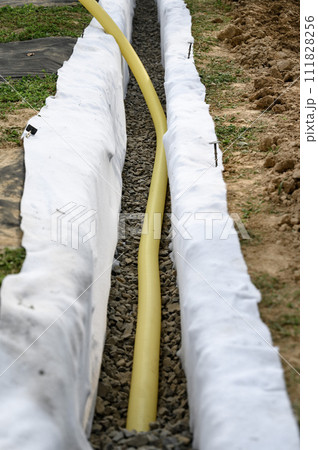 Yellow corrugated pipe with perforation in a trench with crushed stone and geotextile. Drainage works for the removal of ground water. Yellow corrugated pipe with perforation in a trench with crushed stone and geotextile. Drainage works for the removal of ground water. 111828256
