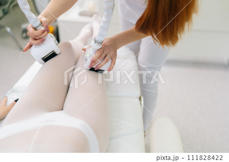 Top view of unrecognizable female patient wearing white suit having anti-cellulite LPG massage. Professional woman masseur doing massage with LPG apparatus machine for lifting body in beauty salon. 111828422