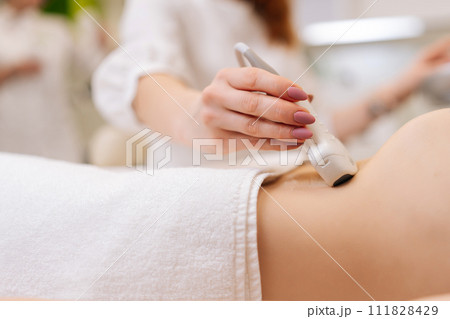 Close-up belly of unrecognizable young woman undergoes ultrasound diagnostics of abdominal organs in modern clinic. Professional doctor doing stomach sonography checkup using medical equipment. 111828429