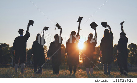 Silhouettes of college graduates waving their caps at sunset. Silhouettes of college graduates waving their caps at sunset. 111828626