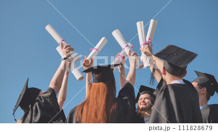 College graduates with caps tie their diplomas together. 111828679