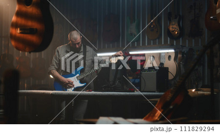 Male craftsman plays guitar connected to combo amp, checks the sound Male craftsman plays guitar connected to combo amp, checks the sound 111829294