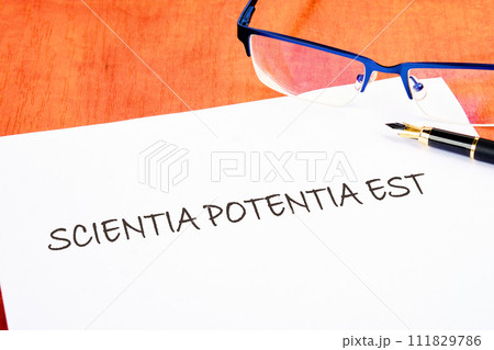 the phrase Scientia Potentia Est (Knowledge is power) written in Latin on a white piece of paper on the table next to the glasses the phrase Scientia Potentia Est (Knowledge is power) written in Latin on a white piece of paper on the table next to the glasses 111829786