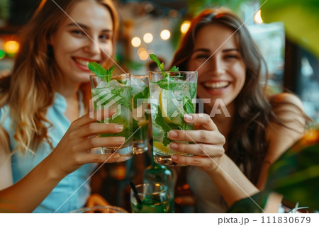 Two women are smiling and toasting with alcoholic beverages at a restaurant 111830679