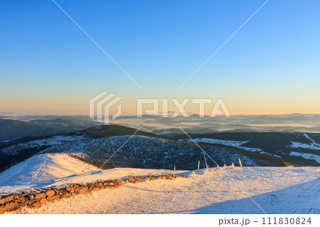 Winter, sunrise time, view from Snezka to pink mountain, krkonose mountain, Czech republic.. Along the road are wooden long bars, tourist markings for winter season. 111830824