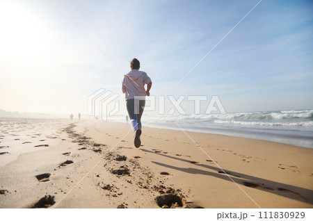 View from the back of a sportive athletic woman running on the sandy beach, during her morning cardio workout View from the back of a sportive athletic woman running on the sandy beach, during her morning cardio workout 111830929