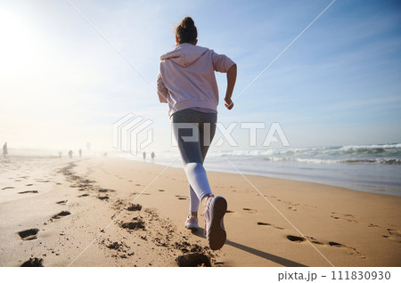 Determined strong young athletic woman, athlete, sportswoman during morning jog, running outdoors along Atlantic beach Determined strong young athletic woman, athlete, sportswoman during morning jog, running outdoors along Atlantic beach 111830930