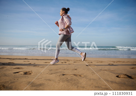 Full length side portrait of a sportive woman exercising outdoor, running jogging on the sandy beach on warm sunny day Full length side portrait of a sportive woman exercising outdoor, running jogging on the sandy beach on warm sunny day 111830931