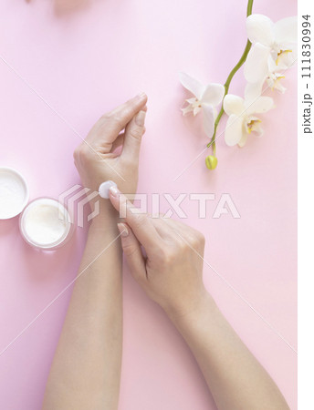 Advertising of cosmetic cream. Hand cream, a woman smears her hands with cream on the background of white orchids. 111830994