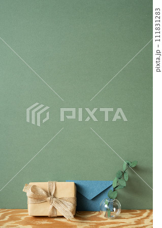 Kraft paper gift box, blue envelope, eucalyptus on wooden table. green wall background 111831283