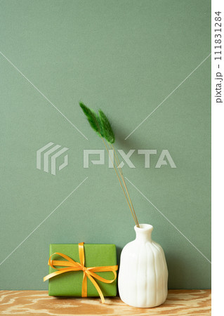 Green gift box and vase of dry flower on wooden table. green wall background Green gift box and vase of dry flower on wooden table. green wall background 111831284