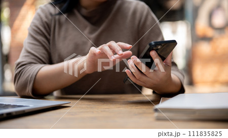 A cropped shot of an Asian woman responding to messages on her smartphone while sitting in a cafe. A cropped shot of an Asian woman responding to messages on her smartphone while sitting in a cafe. 111835825