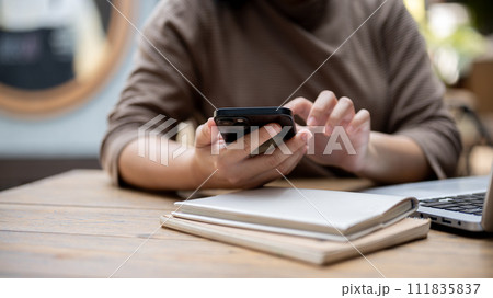 A cropped shot of an Asian woman responding to messages on her smartphone while sitting in a cafe. A cropped shot of an Asian woman responding to messages on her smartphone while sitting in a cafe. 111835837
