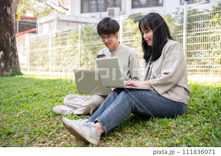 Two young Asian college students are discussing work and using their laptop at a campus park. Two young Asian college students are discussing work and using their laptop at a campus park. 111836071