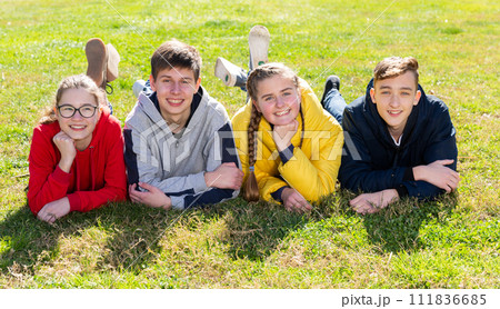Cheerful teen friends lying on green lawn Cheerful teen friends lying on green lawn 111836685