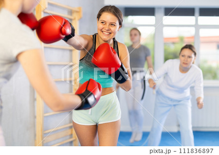 Adolescent girl in boxing gloves practicing punches in sparring during self defence course Adolescent girl in boxing gloves practicing punches in sparring during self defence course 111836897