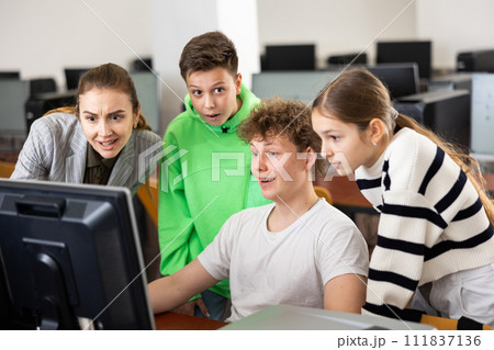 Female teacher and teen students looking at monitor screen during lesson 111837136