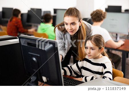 Female teacher talking to focused teen girl student in computer class Female teacher talking to focused teen girl student in computer class 111837149