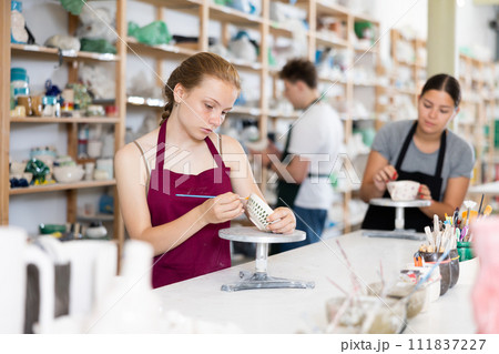 Teenage girl painting ceramic cup in ceramic workshop Teenage girl painting ceramic cup in ceramic workshop 111837227