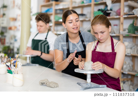 Potter helps young apprentices mold pottery from clay in workshop 111837318
