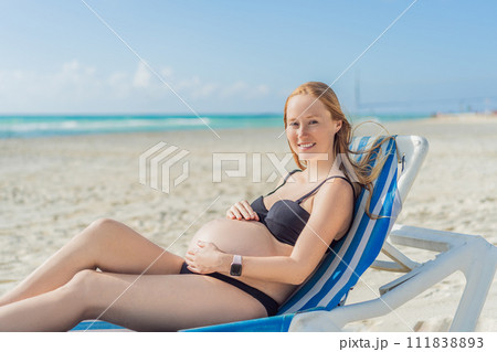 Basking in seaside tranquility, a pregnant woman lounges on a sun lounger, embracing the soothing ambiance of the beach for a moment of serene relaxation Basking in seaside tranquility, a pregnant woman lounges on a sun lounger, embracing the soothing ambiance of the beach for a moment of serene relaxation 111838893