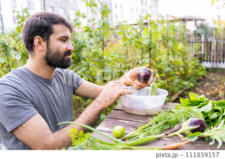 Man is washing carrot and leafy vegetables in plastic container on table Man is washing carrot and leafy vegetables in plastic container on table 111839157