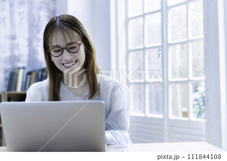 日差しが差し込む明るい部屋でノートパソコンを使う若い女性 111844108
