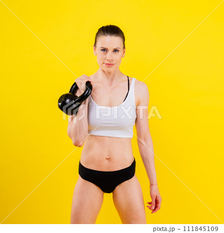 Woman in sportswear doing crossfit workout with kettle bell on dark yellow red background. 111845109