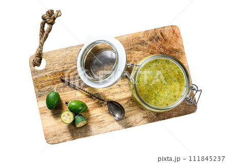 Green feijoa jam on a wooden chopping Board in a glass jar. Isolated on white background. Top view. 111845237