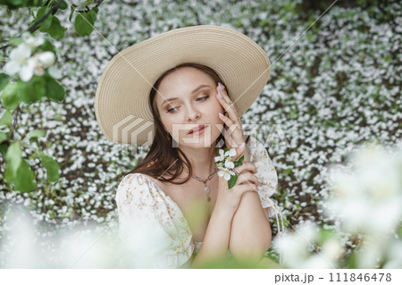 An attractive long-haired woman walks in the spring in the park of blooming apple trees. An attractive long-haired woman walks in the spring in the park of blooming apple trees. 111846478