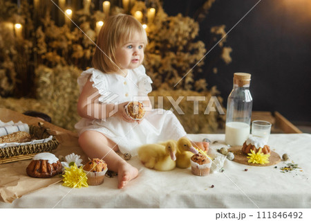 A little girl is sitting on the Easter table and playing with cute fluffy ducklings. The concept of celebrating happy Easter. 111846492