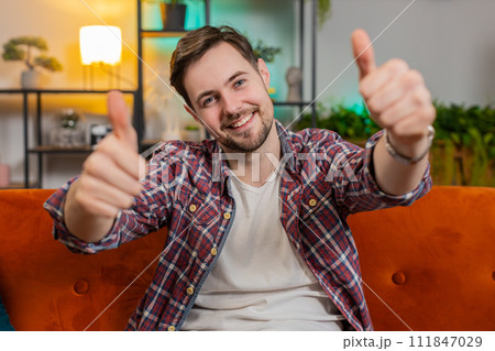 Happy man looking approvingly at camera showing double thumbs up like sign positive feedback at home 111847029