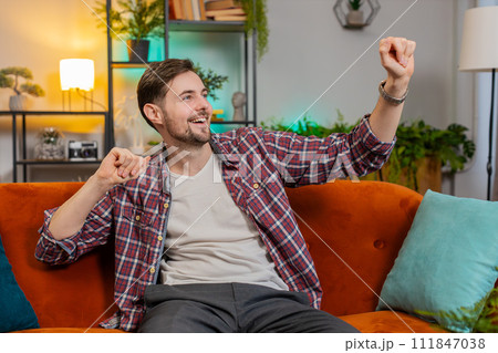 Man singing and dancing celebrate victory win enjoying music sitting on couch in living home room 111847038
